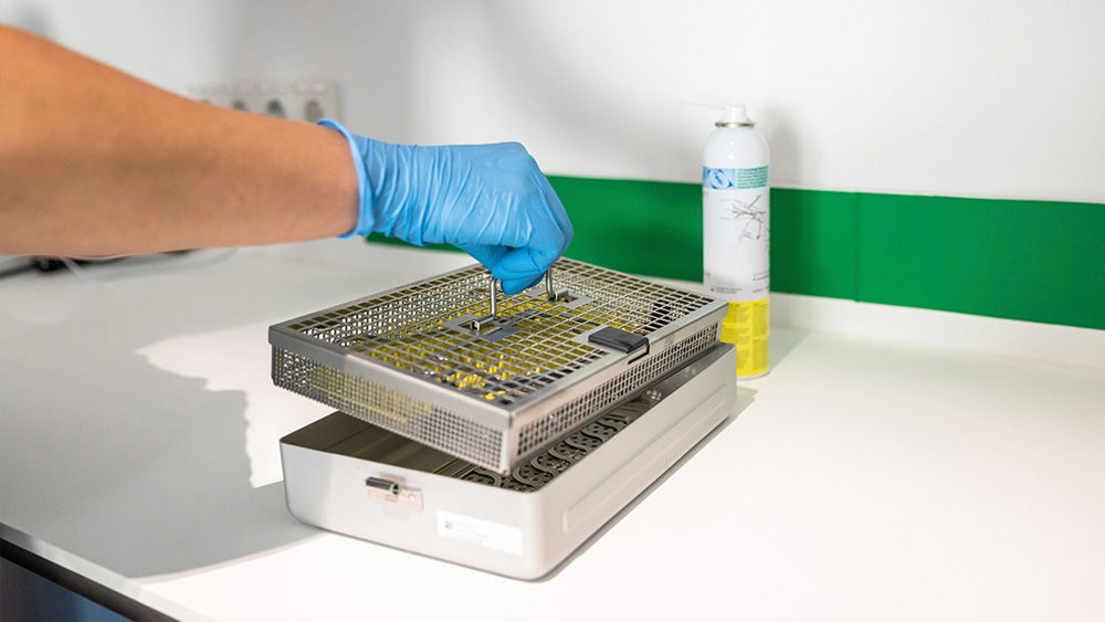 Eine Tiermedizinische Fachangestellte .. hebt ein Instrumentensieb aus einem AESCULAP Sterilcontainer... auf einer hygienischen Arbeitsfläche.