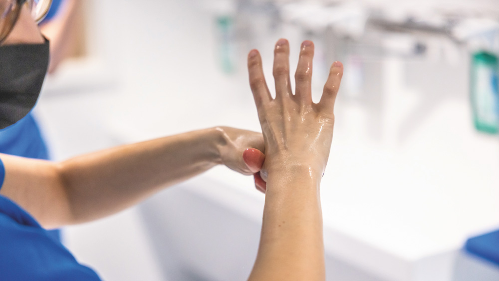 Person reibt Hände mit Desinfektionsmittel im Rahmen der Handhygiene in einer klinischen Umgebung.