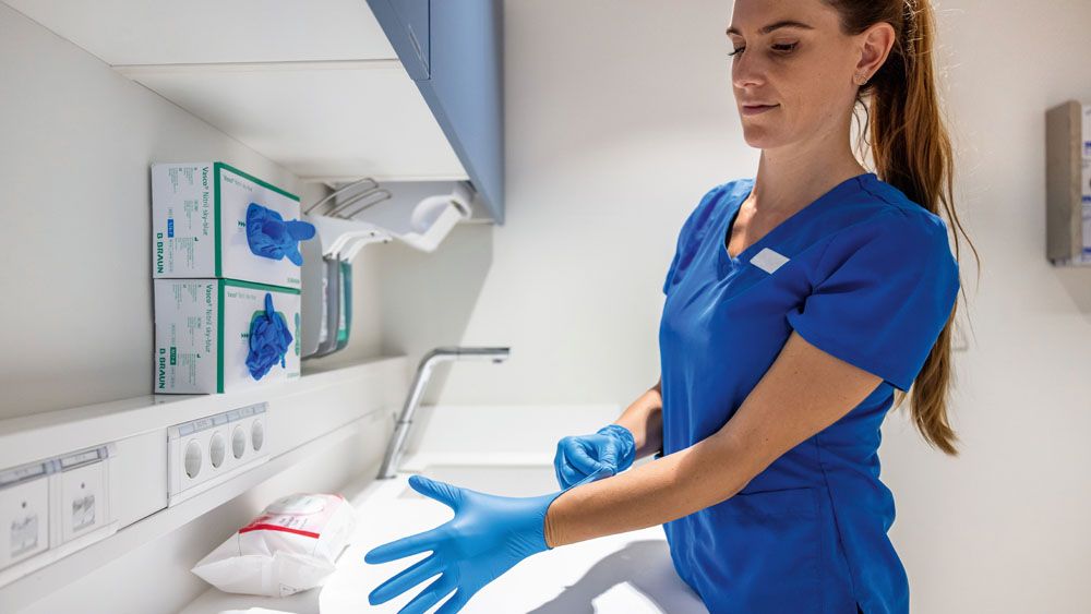 Eine tiermedizinische Fachangestellte in einem klinischen Arbeitsbereich legt Einweghandschuhe an neben organisierten medizinischen Vorräten.