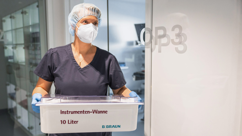 Alt text: Person in Servicekleidung arbeitet mit einem Aesculap‑Sterilisationscontainer in einer klinischen Umgebung.